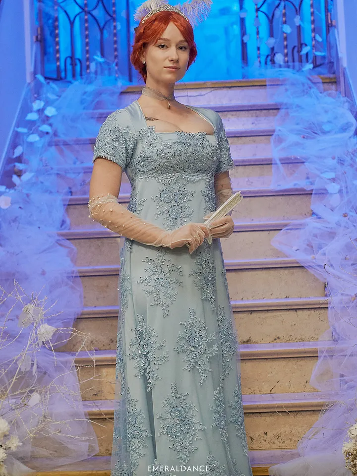 Mujer frente a una escalera con vestido celeste largo bordado, mangas cortas, guantes transparentes y abanico sostenido entre las manos.