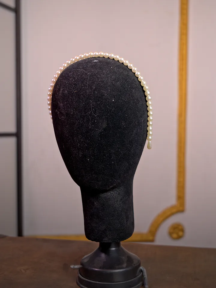 Delgada diadema cubierta de pequeñas perlas claras, vista de perfil sobre una cabeza de maniquí negra.