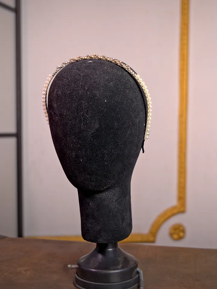 Diadema metálica delgada sobre soporte negro, de tono dorado envejecido y contorno sencillo, sin piedras ni adornos prominentes.