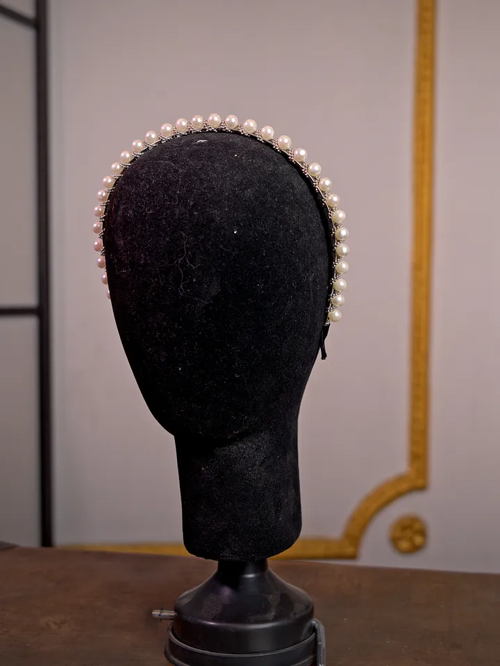 Diadema sencilla cubierta por una hilera uniforme de perlas blancas, presentada sobre un soporte de terciopelo negro.