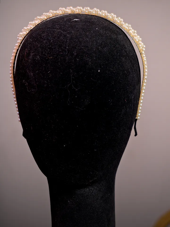 Primer plano de una diadema angosta cubierta por dos hileras de pequeñas perlas claras sobre cabeza de maniquí.