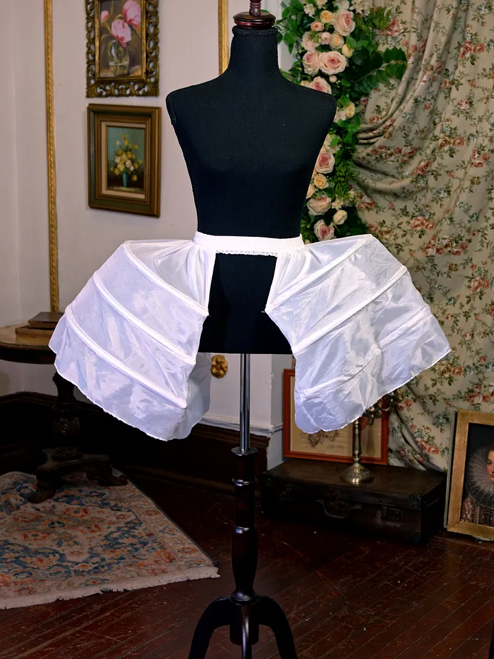 Estructura blanca para dar volumen lateral a una falda, montada sobre maniquí y formada por cintas, paneles y soportes rígidos.