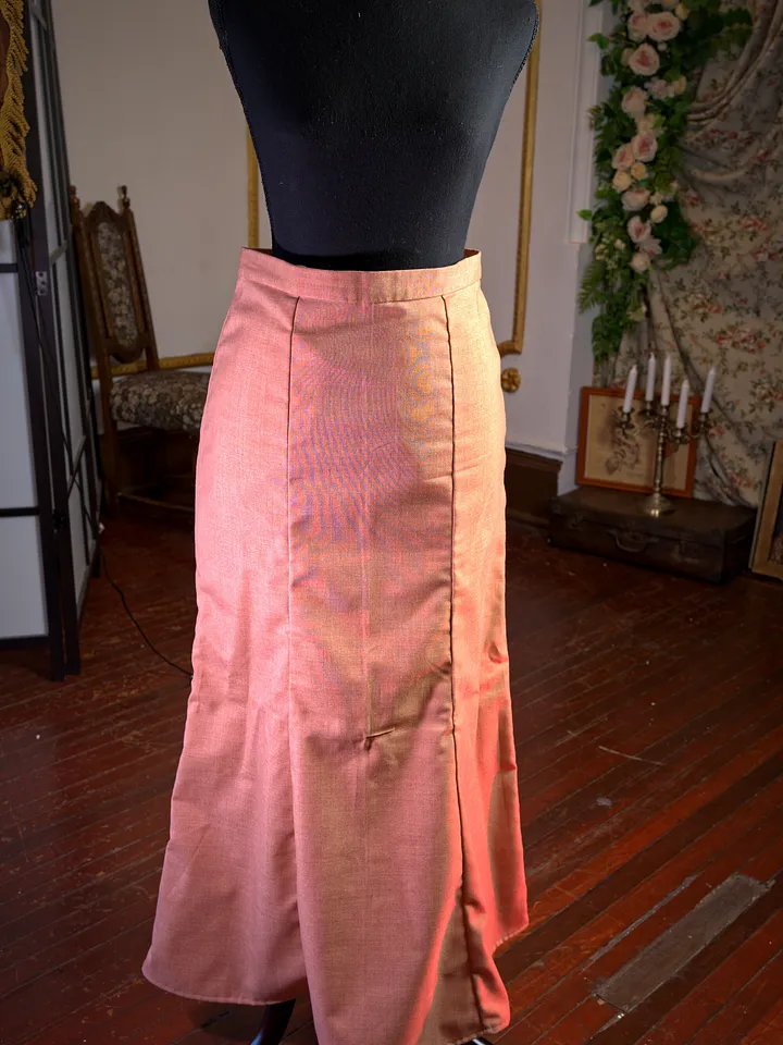 Falda larga color coral sobre maniquí, de cintura alta y corte levemente acampanado, con abertura formada por paneles delanteros.