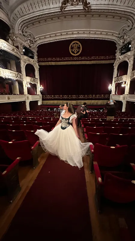 Modelo usando el vestido Annie en un teatro, con corpiño verde bordado, mangas de encaje y falda blanca de tul amplia entre butacas rojas.