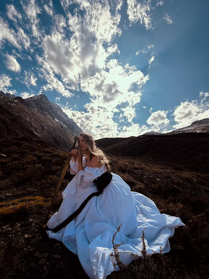 Mujer posando entre rocas con vestido de falda blanca voluminosa y corpiño oscuro, rodeada por un paisaje montañoso.