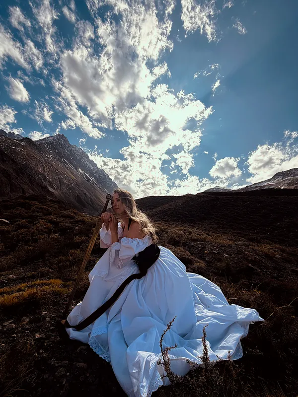 Mujer posando entre rocas con vestido de falda blanca voluminosa y corpiño oscuro, rodeada por un paisaje montañoso.