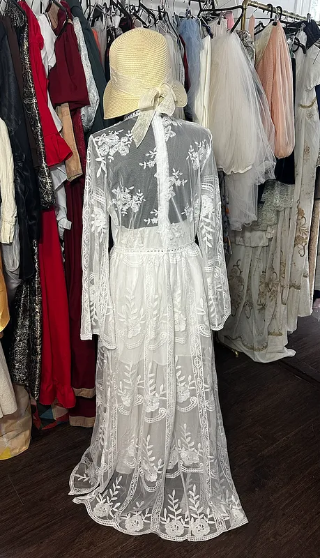 Vista posterior del vestido blanco, con espalda y mangas de encaje floral transparente y falda larga de motivos bordados.