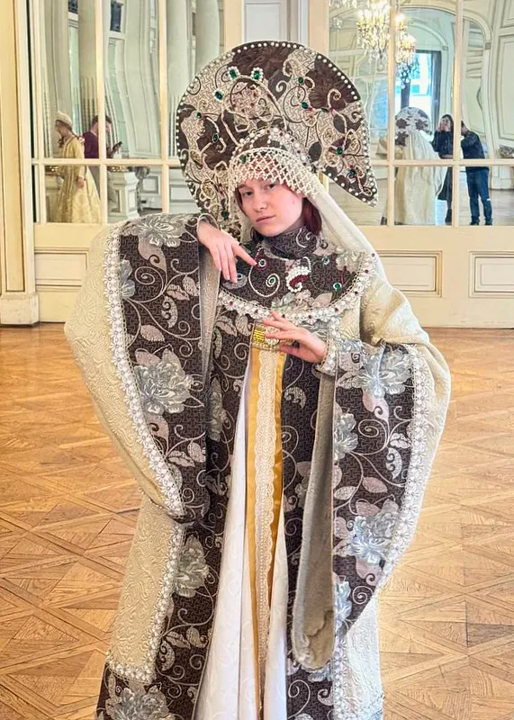 Plano medio del traje en uso, donde se aprecian el brocado floral oscuro, las aplicaciones perladas, el velo claro y el tocado con piedras verdes.