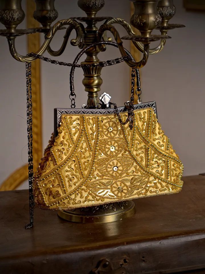 Bolso estructurado de brocado dorado, con motivos ornamentales, marco metálico y dos asas cortas sobre una superficie oscura.