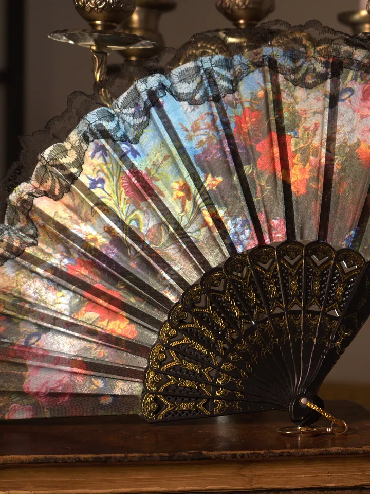 Abanico plegable abierto con varillas oscuras caladas y paneles estampados con flores multicolores sobre fondo claro.